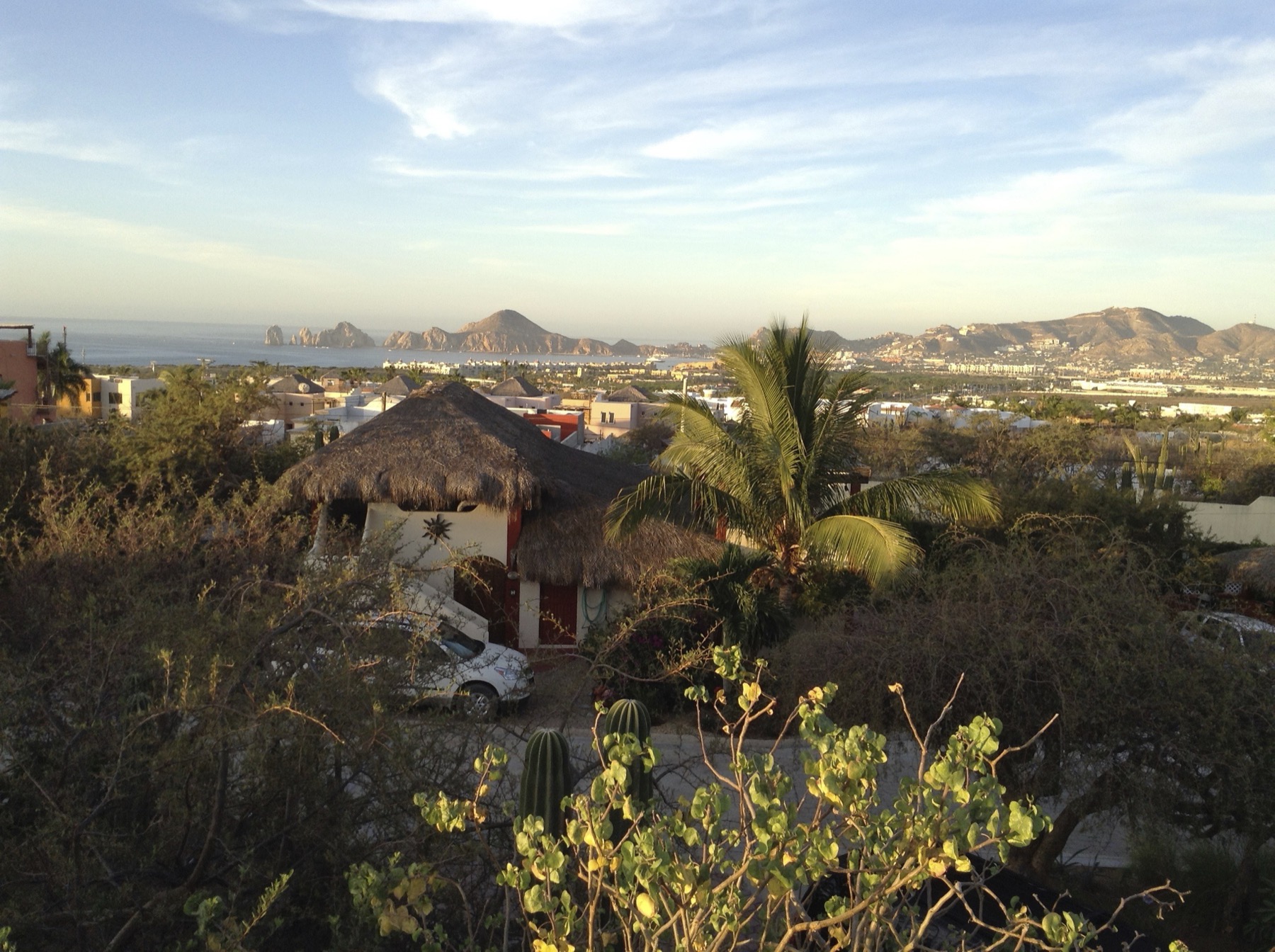 Palapa-roofed home on a hillside above Cabo San Lucas, with the ocean and Land's End rock formations visible in the distance