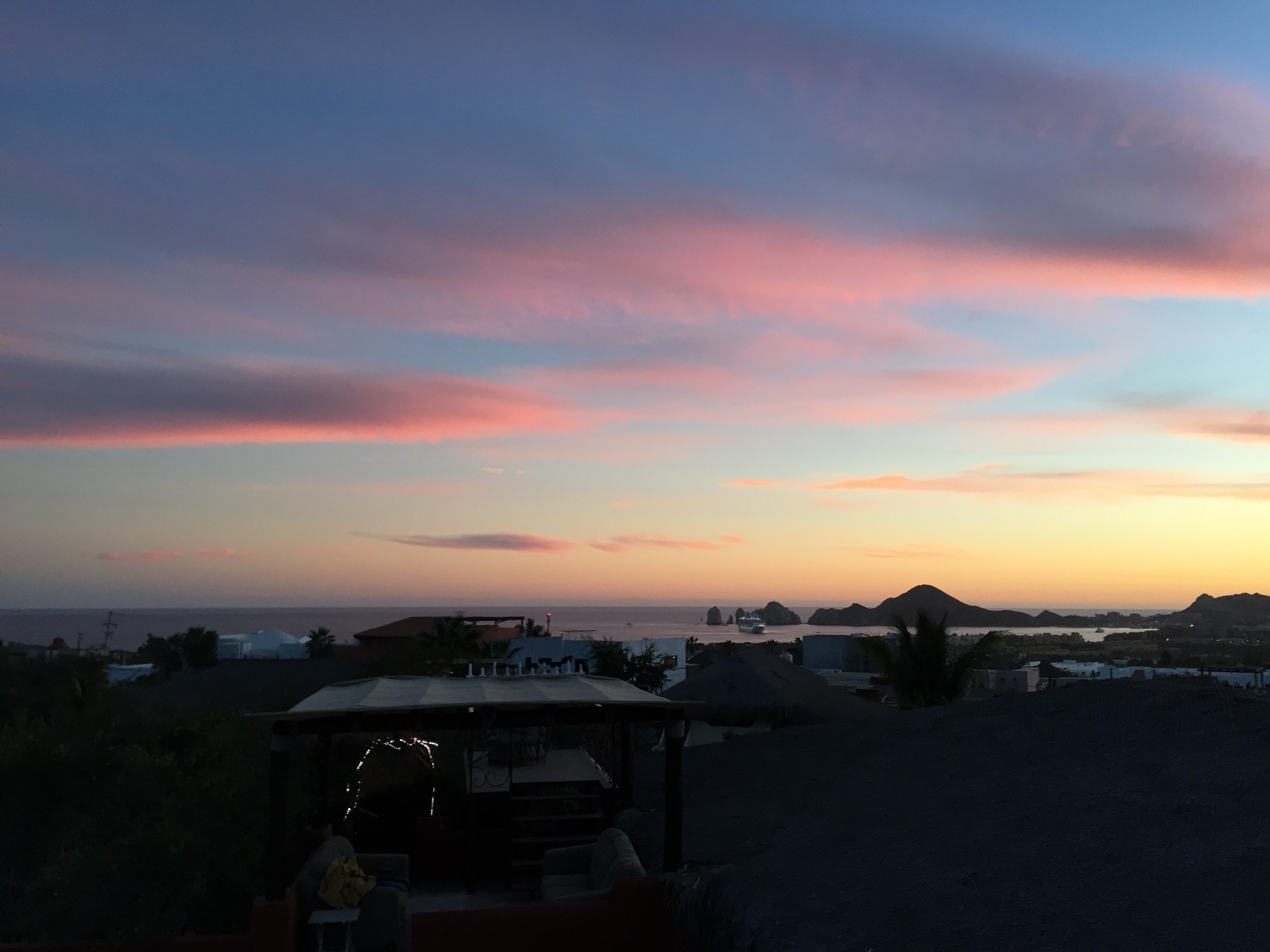 Sunset view from the terrace over the Cabo San Lucas marina, with the Land's End rock arches and a cruise ship visible on the horizon